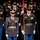 Lt. Gen. Dana Kyle Chipman retirement ceremony A formal U.S. Army military ceremony featuring soldiers in dress uniforms standing in formation. Two central figures appear to be officers or senior NCOs, with one carrying a unit guidon on a red and gold staff. The soldiers are wearing Class A dress uniforms with medals, ribbons, and white gloves, suggesting a ceremonial or parade event.