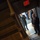 Lt. Gen. Dana Kyle Chipman retirement ceremony The image is taken from above, looking down a dark stairwell toward a doorway. A military officer in full dress uniform and a civilian in a dark suit with a red tie are visible near the doorway threshold. An illuminated red EXIT sign is prominently visible above the door.