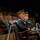 Lt. Gen. Dana Kyle Chipman retirement ceremony Two senior U.S. Army general officers in dress uniforms are seated in the foreground at what appears to be a formal military ceremony or event. Both wear service caps with gold braid ('scrambled eggs') indicating general officer rank, and their uniforms display multiple unit patches and insignia. A large audience of military personnel and civilians is visible in the background.