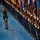 Lt. Gen. Dana Kyle Chipman retirement ceremony A formal military ceremony featuring a long line of uniformed personnel holding flags and guidons on a polished blue floor. A single officer in dress uniform stands at attention in the foreground, holding a ceremonial saber at his side. The formation extends deep into the background, creating a strong sense of depth and discipline.