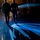 Lt. Gen. Dana Kyle Chipman retirement ceremony Two military personnel in formal dress uniforms are walking away from the camera across a polished floor, illuminated by dramatic blue and warm stage lighting. Their elongated shadows are cast across the reflective surface in a striking geometric pattern. The image appears to capture a ceremonial or formal military event taking place indoors.