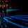 Lt. Gen. Dana Kyle Chipman retirement ceremony Two military officers in formal dress uniforms and peaked caps walk away from the camera across a darkened stage, illuminated by a dramatic spotlight that casts long parallel shadows on the reflective floor. An audience of uniformed personnel and civilians is visible in the background, with some individuals applauding. The scene appears to be a formal military ceremony or change-of-command event held in a large auditorium or arena.