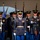 Lt. Gen. Dana Kyle Chipman retirement ceremony A formal U.S. Army ceremonial unit is performing a military drill or parade, with soldiers in dress blue uniforms standing in precise formation. The lead officer in the foreground wears a decorated dress uniform with multiple medals, ribbons, and a gold belt, carrying a ceremonial sword. Multiple color guard members holding rifles with fixed bayonets and unit guidon flags are visible in the background.