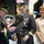 Lt. Gen. Dana Kyle Chipman retirement ceremony A formal U.S. Army military ceremony is taking place, likely a retirement or award presentation. Two senior Army generals in dress uniforms are reviewing a document or citation from a black folder, while a civilian woman wearing a medal stands nearby smiling. Historical uniform re-enactors and military color guard flags are visible in the background.