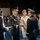 Lt. Gen. Dana Kyle Chipman retirement ceremony A formal U.S. Army military ceremony is taking place, likely a retirement or change of command ceremony. A senior officer in dress blues is receiving or presenting a folded American flag to another officer, while a woman in a white dress stands nearby. Soldiers in historical uniforms are visible in formation in the background.