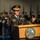 Lt. Gen. Dana Kyle Chipman retirement ceremony A senior U.S. Army officer identified by nameplate as 'DEMPSEY' is delivering a speech at a formal military ceremony. He stands at a wooden podium bearing the official seal of the Department of the Army, United States of America, with both hands raised in an expressive gesture. In the blurred background, rows of uniformed soldiers in dress uniforms and military color guard flags are visible.