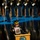 Lt. Gen. Dana Kyle Chipman retirement ceremony A senior U.S. Army officer in dress uniform stands at a Department of the Army podium, holding up a photograph of a soldier in combat gear. Behind him, a formation of uniformed soldiers stands at attention on a blue-lit stage, holding rifles. The setting appears to be a formal military ceremony or official event.