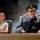 Lt. Gen. Dana Kyle Chipman retirement ceremony A high-ranking U.S. Army officer in full dress uniform is seated alongside a woman wearing a white outfit and a medal, likely at a formal military ceremony. The officer displays numerous service ribbons, gold insignia, and a peaked cap with general officer ornamentation. Flags and an auditorium-style setting are visible in the background.