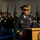 Lt. Gen. Dana Kyle Chipman retirement ceremony A U.S. Army general officer is delivering a speech at a formal military ceremony, standing at a wooden podium bearing the Department of the Army seal. The officer, identified by a name tag reading 'CHIPMAN,' wears dress blues with general officer rank insignia and multiple service ribbons and medals. A military honor guard in ceremonial uniforms is visible in the blurred background.