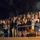 Lt. Gen. Dana Kyle Chipman retirement ceremony A large crowd of people is standing and applauding in what appears to be an auditorium or theater balcony section. The gathering appears to be a formal ceremony or event, likely a graduation, awards ceremony, or similar celebratory occasion. Several individuals in the foreground are dressed formally and some are holding flowers, programs, or awards.