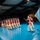 Lt. Gen. Dana Kyle Chipman retirement ceremony A ceremonial military drill team dressed in 18th-century Continental Army uniforms marches in formation on a blue-floored indoor venue. A lead soldier carries a light blue flag adorned with white stars and gold fringe, likely representing a U.S. Army ceremonial unit. The event appears to be a formal military ceremony or gala held in a large event hall.