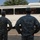 81st Civil Affairs Battalion welcome home ceremony Two military personnel in US Army ACU (Army Combat Uniform) digital camouflage stand with hands on hips, facing a large white Blue Bird All American bus filled with soldiers. The scene appears to be a military transport or deployment situation, likely on a military installation. The two individuals in the foreground appear to be in a supervisory or observational role.