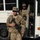 81st Civil Affairs Battalion welcome home ceremony Two U.S. Army soldiers in MultiCam (OCP) camouflage uniforms are disembarking from a Blue Bird bus. The foreground soldier carries an M4 carbine rifle and wears an ISAF patch, indicating deployment to or from Afghanistan. The background soldier, identified by nametape as 'WHITAKER,' holds what appears to be a folded ACU-pattern garment.
