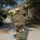 81st Civil Affairs Battalion welcome home ceremony A U.S. Army soldier in MultiCam (OCP) camouflage uniform is walking away from the camera on a sidewalk at what appears to be a military installation. The soldier is carrying a large MOLLE rucksack on their back and dragging a green duffel bag with identification tags attached. The setting suggests a deployment, arrival, or movement between facilities on a military base.