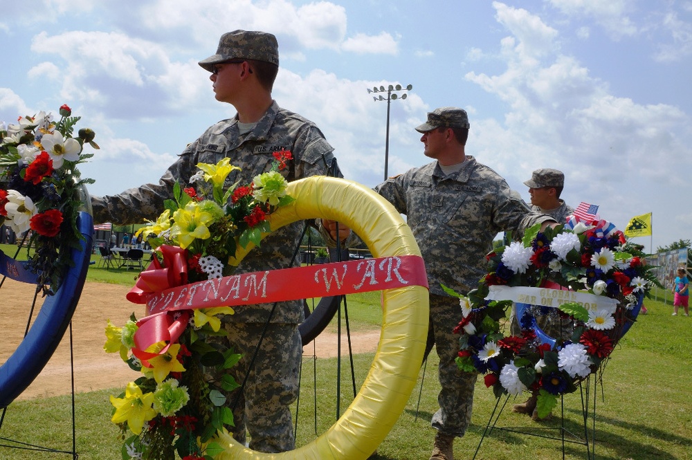 Soldiers look on while holding up commemorative wreaths during a windy ceremony