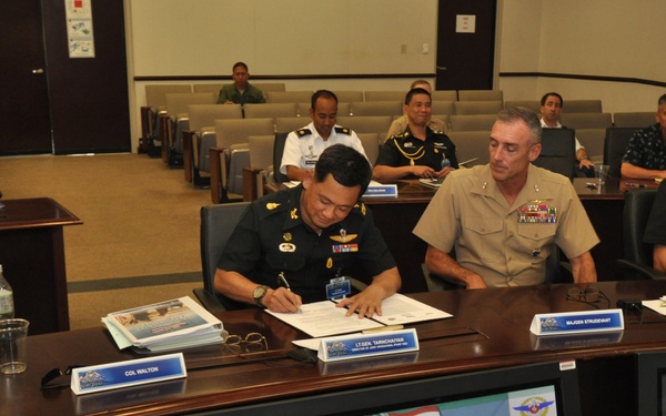 A formal military conference room setting showing U.S. and Thai military officers participating in U.S.-Thailand Senior Staff Talks (SST) in Honolulu, Hawaii. Officers are seated at a curved conference table with name placards visible, including 'COL WALTON,' 'LT GEN TANICHAYAN,' and 'MAJGEN STRUDEVANT.' A presentation screen in the foreground displays the event title with both U.S. and Thai flags.