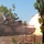 Exercise Gold Eagle smooth ride for Aussie, Marine tanks A main battle tank is captured mid-fire, with a large muzzle blast and fireball visible at the end of the gun barrel. The tank appears to be operating in a dry, sparse woodland environment under clear blue skies. A red flag is visible on the turret, commonly used as a safety marker during live-fire exercises.