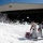 Flurry of foam released at Travis Three personnel are responding to a fire suppression foam discharge event outside a large hangar marked '818'. A massive amount of white firefighting foam covers the ground and is spraying into the air. Two individuals appear to be in military/flight suits while a third wears a white shirt and dark pants, consistent with a fire safety official.