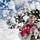 Flurry of foam released at Travis A man is caught in a burst of white foam or artificial snow outdoors, squinting and reacting to the material hitting his face. He is holding a red object, possibly a container or device, and appears to be in a playful or work-related situation. The background shows a blue sky and a building structure partially obscured by the foam.