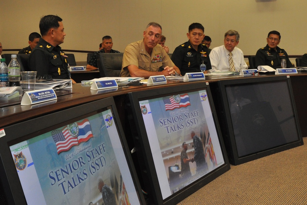 A formal military meeting between U.S. and Thai military officials, identified as 'U.S.-Thailand Senior Staff Talks (SST).' Participants are seated at a conference table with name placards, and multiple monitors in the foreground display the SST title slide featuring both the American and Thai flags. The setting appears to be an official military conference room.