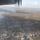 An aerial photograph taken from a fixed-wing aircraft showing a coastal town that has sustained severe damage, consistent with a major tropical cyclone or typhoon strike. The urban area shows widespread structural destruction, with stripped vegetation across the surrounding landscape appearing brown and denuded. Blue tarps are visible on numerous structures, indicating emergency shelter measures in the aftermath of a disaster.