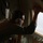 A person wearing aviation headphones is leaning toward a window inside what appears to be a military or cargo aircraft. They appear to be inspecting or working on the window area, possibly performing a maintenance check or visual observation. The interior environment is dimly lit with the window providing the primary light source.