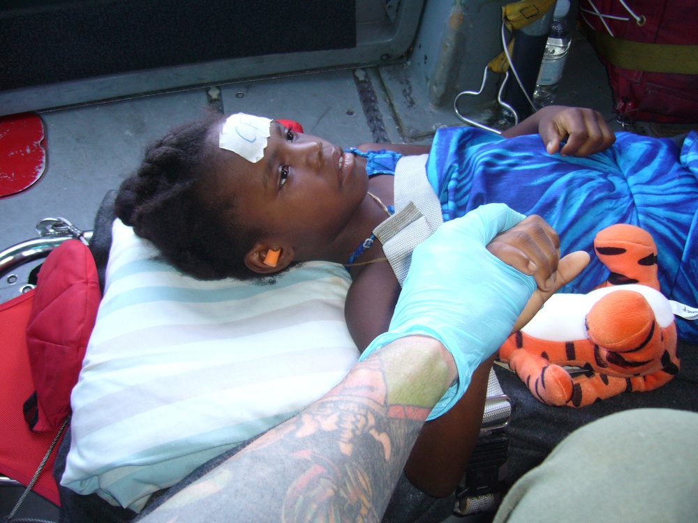 PORT AU PRINCE, Haiti- Petty Officer 2nd Class Duane Zitta holds the hand of a 6-year-old Haitian girl who suffered from compound fractures to the lower left leg January 18, 2010. The MH-65 dolphin helicopter crew from Air Station Detroit, Mich., medevaced nine injured people to a medical facility in Milot, Haiti where they received medical attention from the Red Cross. U.S. Coast Guard photo