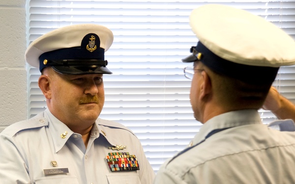 Two U.S. Coast Guard personnel are engaged in a formal military ceremony, likely a retirement or award presentation. The service member facing the camera, identified by nameplate as 'PERCELL,' is holding a folded American flag and wearing dress uniform with multiple ribbons and medals. The second individual, shown from behind, appears to be rendering a salute.