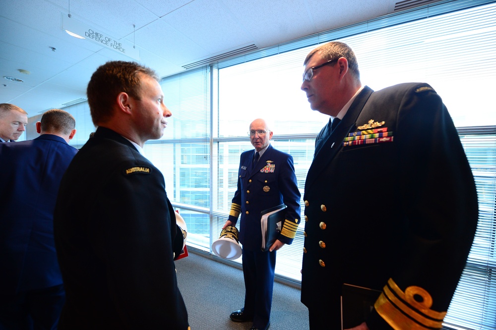 The image shows a group of military officers in formal naval dress uniforms engaged in conversation inside what appears to be an official building. A sign reading 'Chief of the Defence Force' is visible on the ceiling in the background. At least one officer has an 'Australia' shoulder title visible on their uniform.