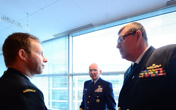 The image shows a group of military officers in formal naval dress uniforms engaged in conversation inside what appears to be an official building. A sign reading 'Chief of the Defence Force' is visible on the ceiling in the background. At least one officer has an 'Australia' shoulder title visible on their uniform.