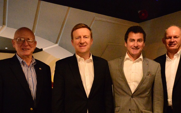 Four men are posing together for a group photo in what appears to be an upscale restaurant or event venue with distinctive arched ceiling architecture and red seating. They are dressed in business casual to business formal attire, suggesting a professional or social gathering. The lighting is warm and dim, typical of an evening dining establishment.