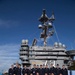 A group of approximately 20-25 military personnel in dark navy dress uniforms are posing for a group photograph on the flight deck of a large aircraft carrier. The island superstructure behind them displays the number '73' and the warning 'BEWARE OF JET BLAST, PROPELLERS, AND ROTORS,' identifying this as USS George Washington (CVN-73). The personnel appear to be members of the Japan Air Self-Defense Force (JASDF) based on their uniform style and insignia.