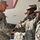 A U.S. Army officer is shaking hands with soldiers in a formal greeting or recognition ceremony outdoors. All personnel are wearing Army Combat Uniforms (ACU) with digital camouflage pattern. The setting appears to be a military installation during winter conditions, visible by snow in the background.