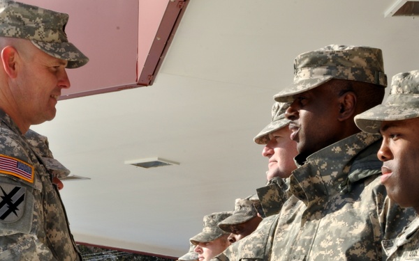 A U.S. Army officer is shaking hands with soldiers in a formal greeting or recognition ceremony outdoors. All personnel are wearing Army Combat Uniforms (ACU) with digital camouflage pattern. The setting appears to be a military installation during winter conditions, visible by snow in the background.
