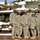 Five U.S. Army soldiers in ACU (Army Combat Uniform) digital camouflage are posing together in front of a static display tank in a snowy outdoor setting. The group appears to be at a military installation or museum, with snow covering the ground, benches, and the tank behind them. The soldiers are smiling and appear to be in a casual group photo.