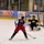 A hockey game is taking place at an indoor ice rink, likely in Alaska based on the rink advertisements. Player number 21 in a navy and red uniform is approaching the goal, facing an 'ARMY' goalie in black and yellow. The scene captures a one-on-one scoring opportunity with spectators visible through the glass in the background.