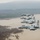 Four A-10 Thunderbolt II (Warthog) attack aircraft fly in a diagonal echelon formation over a flooded river landscape. The aircraft display 'FS' tail codes and Arkansas Air National Guard markings, with the nearest aircraft bearing 'Fort Smith' nose art and a tiger shark mouth painting. The terrain below shows heavily flooded lowlands, bare trees partially submerged in murky water, and forested hills in the background.