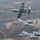 Three A-10 Thunderbolt II (Warthog) aircraft fly in formation over a rural, hilly landscape with sparse winter vegetation. The aircraft appear to belong to the Arkansas Air National Guard, identifiable by the 'FS' tail codes and diamond insignia on the tail fins. The formation includes one aircraft in a slight bank at the top, with two flying level below it.