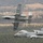 Two U.S. Air Force A-10 Thunderbolt II (Warthog) aircraft flying in formation over a rural landscape with mixed forest and farmland terrain. Both aircraft display 'FS' tail codes indicating assignment to Fort Smith, Arkansas Air National Guard. The lower aircraft features distinctive nose art and Arkansas state markings on the tail.