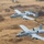 Two A-10 Thunderbolt II (Warthog) aircraft fly in formation over rural farmland terrain. Both aircraft display Arkansas Air National Guard markings with 'FS' tail codes and Fort Smith unit insignia. The aircraft feature distinctive nose art and are photographed from an aerial vantage point, likely from a third aircraft.