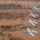 Four A-10 Thunderbolt II (Warthog) aircraft fly in a diagonal echelon formation over a barren, autumnal landscape. The aircraft appear to be U.S. Air Force jets based on visible national insignia and markings. The photograph is taken from an aerial perspective, likely from a fifth aircraft or elevated vantage point.
