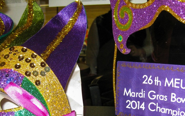 The image shows a Mardi Gras-themed display celebrating the '26th MEU Mardi Gras Bowling 2014 Champions.' The scene features decorative masquerade masks in traditional Mardi Gras colors (purple, gold, and green) alongside gift cards on a dark surface. This appears to be a prize or award display for a military unit (MEU - Marine Expeditionary Unit) bowling championship event.