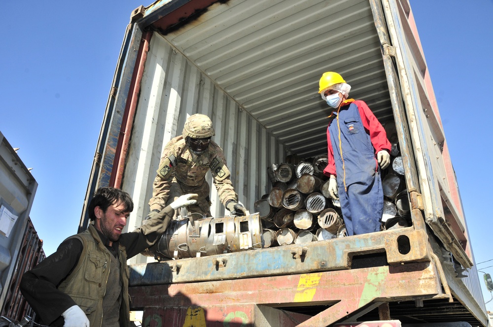 Soldiers and local national workers load a truck with coal burging stoves