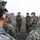 Chaplain exchange promotes brotherhood during MEFEX 2014 A group of military personnel in camouflage uniforms are gathered in an outdoor briefing or discussion circle on a gravel surface. Two individuals in what appears to be US Marine Corps MARPAT woodland camouflage are addressing a group wearing a different digital camouflage pattern, suggesting a multinational or joint military exercise. The setting appears to be a training area or military installation with bare trees and overcast skies in the background.