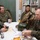 Chaplain exchange promotes brotherhood during MEFEX 2014 Four military personnel — two in US Marine Corps/Navy camouflage uniforms and two in Republic of Korea (ROK) Army uniforms — are seated or standing around a white table in what appears to be an office or library setting. They appear to be engaged in a meeting or exchange, with items including beverages, snacks, documents, and military gear visible on and around the table. A bag labeled 'CHAPLAIN OWEN' is prominently placed on the table, suggesting a chaplain-related bilateral military engagement.