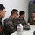 Chaplain exchange promotes brotherhood during MEFEX 2014 A meeting is taking place between a Western military officer in MARPAT (US Marine Corps) camouflage and three personnel wearing Korean military camouflage uniforms, seated around a white table. The Western officer appears to be briefing or discussing something while gesturing with his hand. The setting appears to be an indoor military office or briefing room.