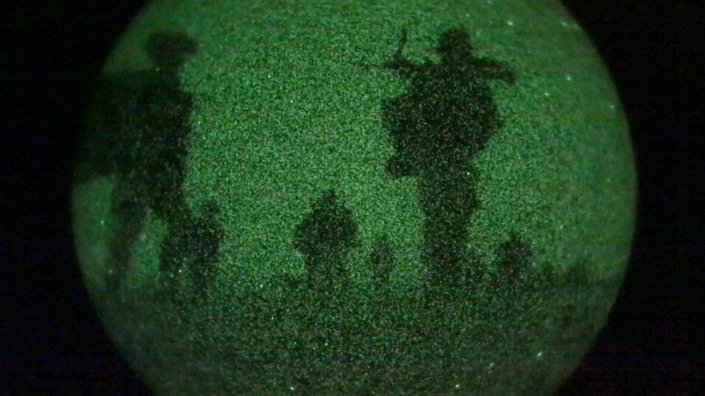 A green glittery or sand-coated spherical object is photographed against a black background. The surface of the sphere displays dark silhouette impressions of human figures and what appears to be a helicopter, embedded or pressed into the green granular material. The overall aesthetic suggests a decorative or artistic object, possibly a bath bomb or sand-art sphere.