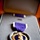 A Purple Heart military medal is displayed in its official presentation case. The medal features a gold-bordered purple heart shape with a profile relief of George Washington and his coat of arms at the top, suspended from a purple ribbon with white edges. The case also contains a service ribbon bar and a lapel pin in the upper portion.