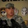 A U.S. Army officer in Army Combat Uniform (ACU) digital camouflage pattern is speaking at a press conference, standing before a backdrop displaying multiple military unit insignia patches. The officer's cap displays three stars, indicating the rank of Lieutenant General. Multiple microphones are positioned in the foreground, suggesting a formal media briefing.