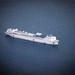 An aerial photograph of a large white hospital ship at sea, identifiable by the prominent red cross markings on its hull. The vessel appears to be stationary or moving slowly in calm, dark blue open water. The ship's all-white paint scheme and multiple red crosses are consistent with a military or international humanitarian hospital ship.